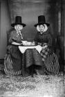 Two women in Welsh national dress, drinking tea...