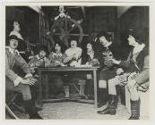 Young men in costume perform around table